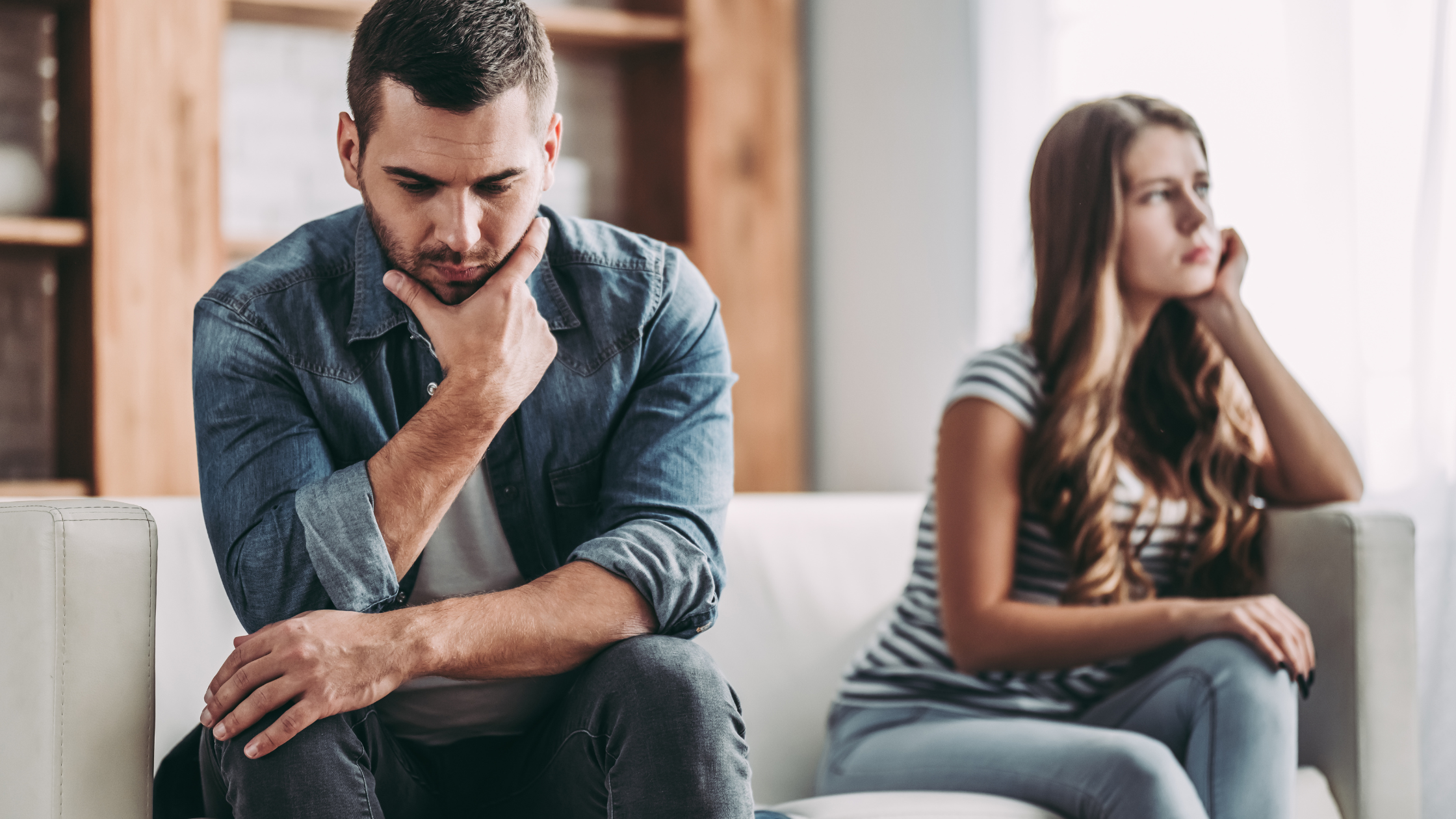 A couple sits on a sofa; the man comforts the woman who is holding a pregnancy test and looks concerned.
